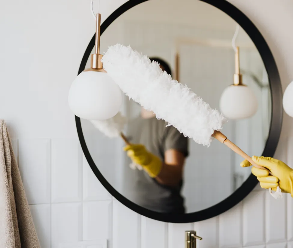 Sweep pea cleaning worker dusting a light fixture in a residential bathroom cleaning service. 