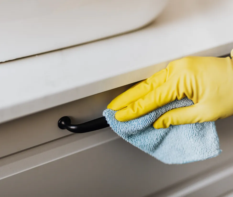 Sweep pea cleaning worker dusting a fixture with a yellow cleaning glove and a professional microfiber cloth to prevent damage to the surface.